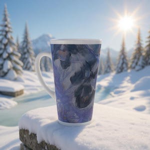 May include: A tall, white-handled latte mug with a blue and purple floral design. The mug is set against a snowy winter landscape with a bright sun and snow-covered trees. The mug's design features a watercolor-like pattern.