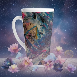 May include: A tall white ceramic latte mug with a large handle. The mug features an abstract design with swirls of blue, pink, gold, and black. The mug is decorated with floral elements and set against a starry background.