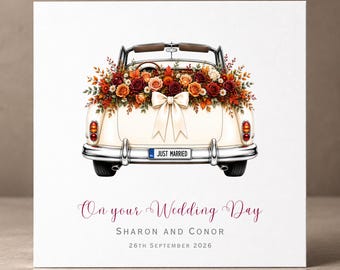 Op de afbeelding: Een vierkante wenskaart met een vintage crèmekleurige cabriolet versierd met rozen en gebladerte in herfsttinten. Een crèmekleurige strik zit op de kofferbak boven een nummerplaat met de tekst JUST MARRIED. Tekst: On your Wedding Day, SHARON AND CONOR, 26TH SEPTEMBER 2026.