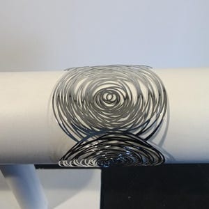 May include: A white cylindrical object with a black and gray spiral design. The design is made of thin, curved lines that create a swirling pattern. The object is on a white surface.