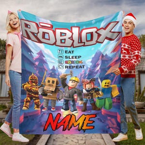 May include: A Roblox blanket with the Roblox logo, the text "EAT SLEEP ROBLOX REPEAT", and Roblox character illustrations. The background is blue and white with a forest scene. The blanket has a space for a custom name.