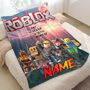 May include: A vibrant Roblox blanket with the Roblox logo and characters. The blanket displays a sunset backdrop and the text "EAT SLEEP ROBLOX REPEAT" along with a space for a name. The blanket is made of soft material.