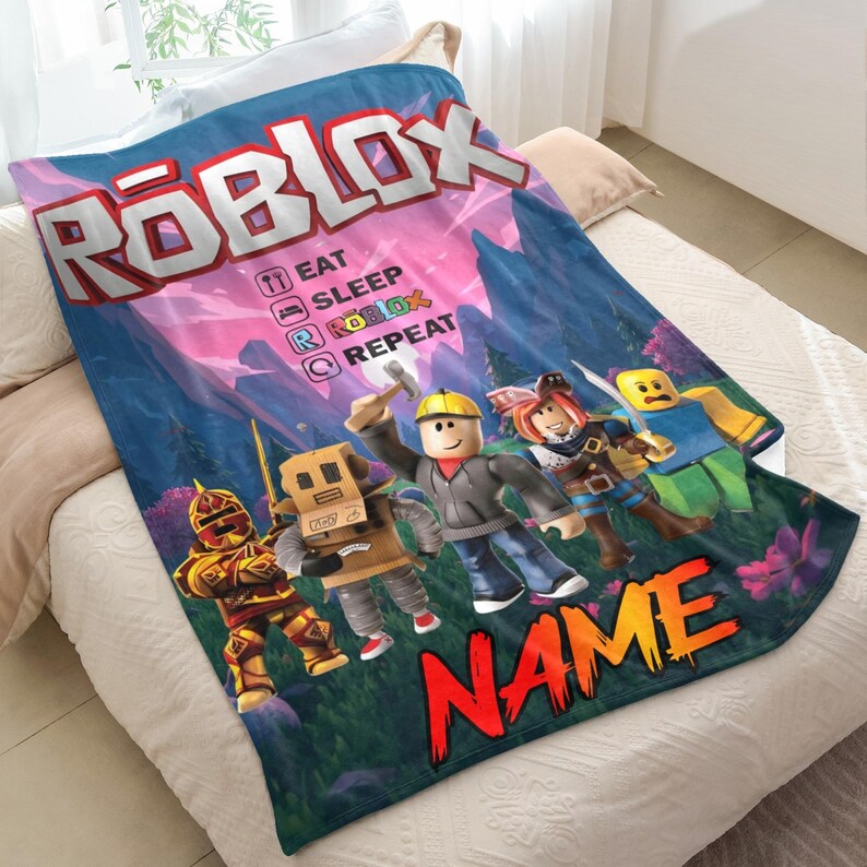May include: A blue blanket with the Roblox logo in white, and the text "EAT SLEEP ROBLOX REPEAT." The blanket displays various Roblox characters and the name "NAME" in orange and red. The background shows a forest scene.