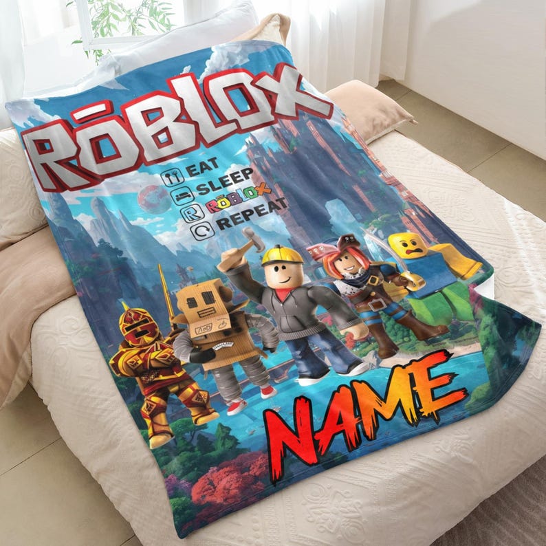 May include: A blue Roblox-themed blanket with the Roblox logo and characters. The blanket has the words "EAT SLEEP ROBLOX REPEAT" and a space for a name. The blanket is on a white bed.