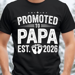 May include: Black t-shirt with the text "PROMOTED TO PAPA EST. 2026" in white, featuring a footprint design. A casual wear item, ideal for a new father.