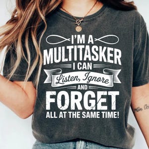 Puede incluir: Camiseta gris oscuro con el texto blanco: "I'M A MULTITASKER I CAN Listen, Ignore AND FORGET ALL AT THE SAME TIME!". La camiseta tiene un aspecto vintage y desgastado.
