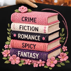May include: A black decorative pillow featuring a stack of crocheted books. The books are labeled "CRIME", "FICTION", "ROMANCE", "SPICY", and "FANTASY". Pink flowers and green leaves surround the books, with a large pink flower at the top.