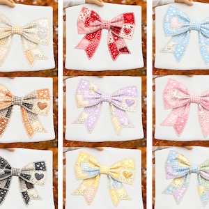Könnte beinhalten: Neun Stoffschleifen in verschiedenen Farben, jede mit einem Patchwork-Design und einem herzförmigen Akzent. Die Schleifen werden auf weißem Hintergrund präsentiert und zeigen eine Reihe von Farben, darunter Beige, Rot, Blau, Orange, Lila, Rosa, Schwarz, Gelb und Pastelltöne.