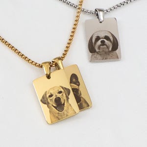Może przedstawiać: Dwa naszyjniki z wisiorkami z motywem psów. Jeden jest w kolorze złotym, z portretem uśmiechniętego psa, a drugi w kolorze srebrnym, z portretem psa. Oba wisiorki są prostokątne i wiszą na delikatnych łańcuszkach.