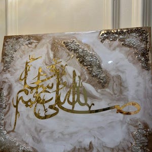 May include: A rectangular artwork featuring gold Arabic calligraphy on a white and brown marbled background. The edges are adorned with silver and gold accents, creating a luxurious aesthetic. The piece is likely a decorative item for home decor.