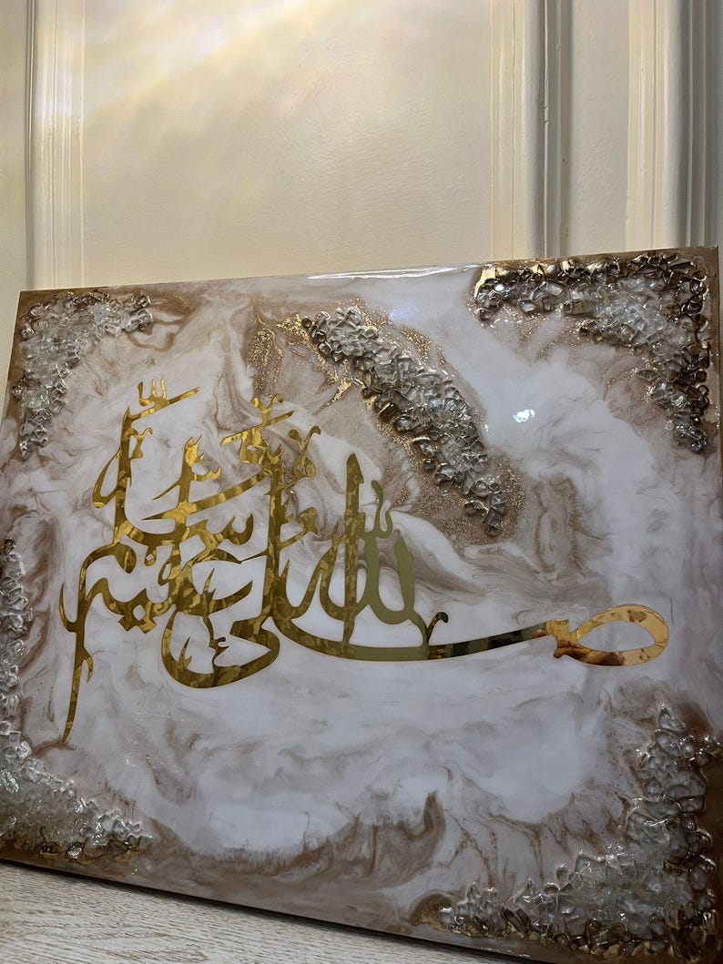 May include: A rectangular artwork featuring gold Arabic calligraphy on a white and brown marbled background. The edges are adorned with silver and gold accents, creating a luxurious aesthetic. The piece is likely a decorative item for home decor.