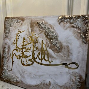 May include: A rectangular wall art piece with gold Arabic calligraphy on a white and brown marbled background. The edges are decorated with silver and clear textured accents. The artwork is a decorative piece.