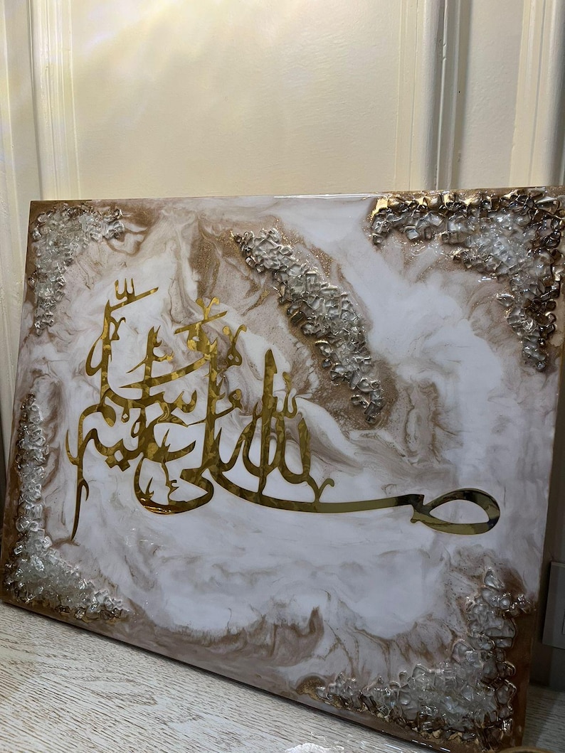 May include: A rectangular wall art piece with gold Arabic calligraphy on a white and brown marbled background. The edges are decorated with silver and clear textured accents. The artwork is a decorative piece.