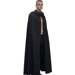 Może przedstawiać: Długi, czarny płaszcz z drapowanym kołnierzem. Peleryna sięga do ziemi i jest wykonana z zwiewnej tkaniny. Osoba ma na sobie czarne spodnie. Tło jest jednolicie białe.