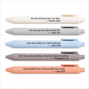 May include: A set of five retractable ballpoint pens in matte pastel colors including cream, gray, light blue, taupe, and peach. Each pen features a unique Bible verse printed in black text along the barrel and a matching plastic pocket clip.