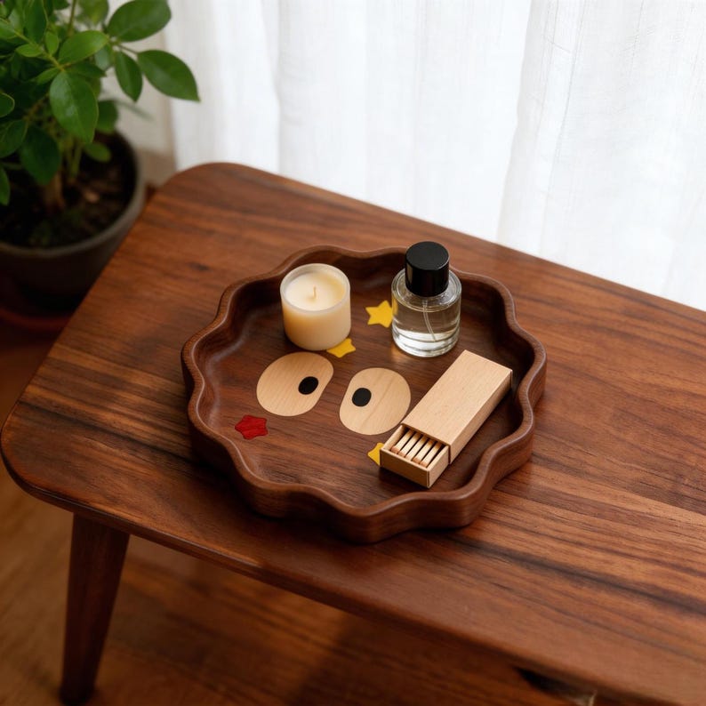 May include: A wooden tray with a wavy edge, featuring a whimsical face design with wooden eyes and a red mouth. The tray holds a lit candle, a small perfume bottle, a matchbox, and star-shaped decorations. The tray is on a wooden table.