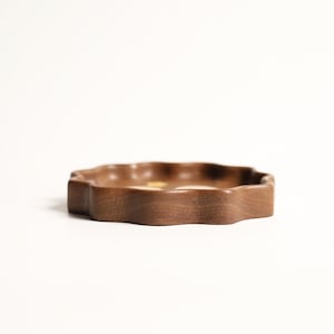 May include: A wooden, wavy-edged tray in a warm brown hue. The tray has a low profile and a smooth, polished surface. The design is organic and natural, suitable for serving or display.