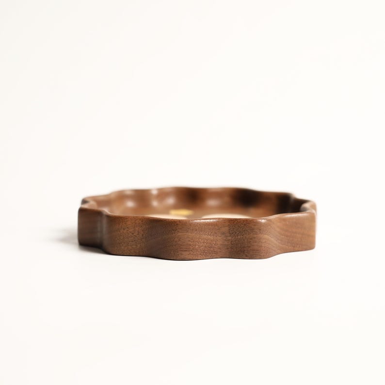 May include: A wooden, wavy-edged tray in a warm brown hue. The tray has a low profile and a smooth, polished surface. The design is organic and natural, suitable for serving or display.