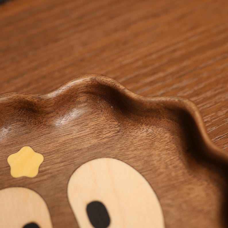 May include: A wooden serving tray with a bear face design. The tray is made of dark brown wood and features a light-colored star and bear face details. The edges of the tray have a wavy, scalloped design.