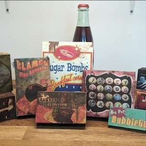 Puede incluir: Una colección de cajas de estilo vintage y una botella con etiquetas retro. Las cajas presentan textos como "Sugar Bombs", "Gumdrops" y "BubbleGum". La paleta de colores incluye marrones, rojos y azules, evocando una sensación nostálgica.