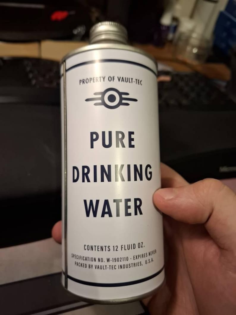 Puede incluir: Una lata cil&iacute;ndrica blanca con la inscripci&oacute;n "PURE DRINKING WATER" y "PROPERTY OF VAULT-TEC". La lata contiene 355 ml. La lata tiene una tapa plateada y un dise&ntilde;o azul y blanco.