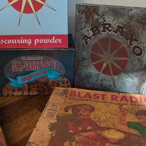 May include: A collection of vintage-style boxes with distressed textures and retro graphics. The boxes feature text like "scouring powder," "All-Vegetarite Shortening," and "Blast Radius." The color palette includes red, green, and yellow.