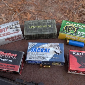 Könnte beinhalten: Verschiedene Munitionskisten, darunter "Dragonfly", "Ballistics", "Jackal", "Heavyfield" und "Red Hawk". Die Kisten sind in verschiedenen Farben und Größen, mit Text und Grafiken. Eine blaue und eine rote Schrotpatrone sind ebenfalls sichtbar.