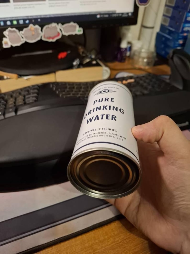 Puede incluir: Una lata blanca y plateada de "Pure Drinking Water" con texto negro. La lata tiene una banda azul y blanca en la parte superior e inferior. La lata contiene 355 ml de agua.