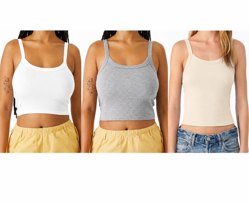 May include: Three cropped tank tops in white, grey, and beige. The white tank top has spaghetti straps and a scoop neckline. The grey tank top has a racerback design. The beige tank top has thin straps and a scoop neckline. All three tops are made of a ribbed material.