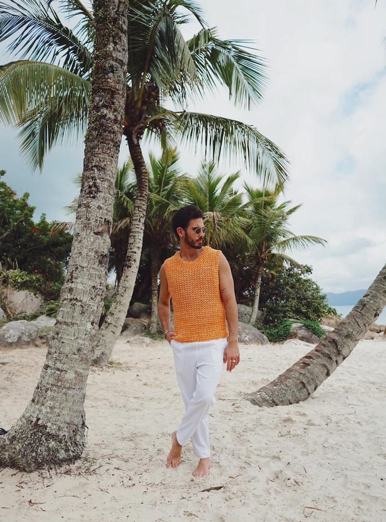 Pu&ograve; includere: Un maglione in maglia senza maniche di colore arancione brillante con scollo rotondo e consistenza spessa, abbinato a pantaloni bianchi semplici. Il capo presenta una trama larga e traspirante con un design essenziale e pulito.