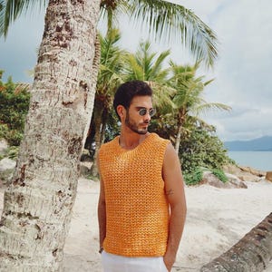 Pu&ograve; includere: Un top smanicato in maglia color arancione brillante con scollo rotondo e un motivo testurizzato a maglia aperta. Il capo &egrave; abbinato a pantaloni bianchi semplici, creando un look essenziale e pulito adatto a climi caldi e ambienti esterni.