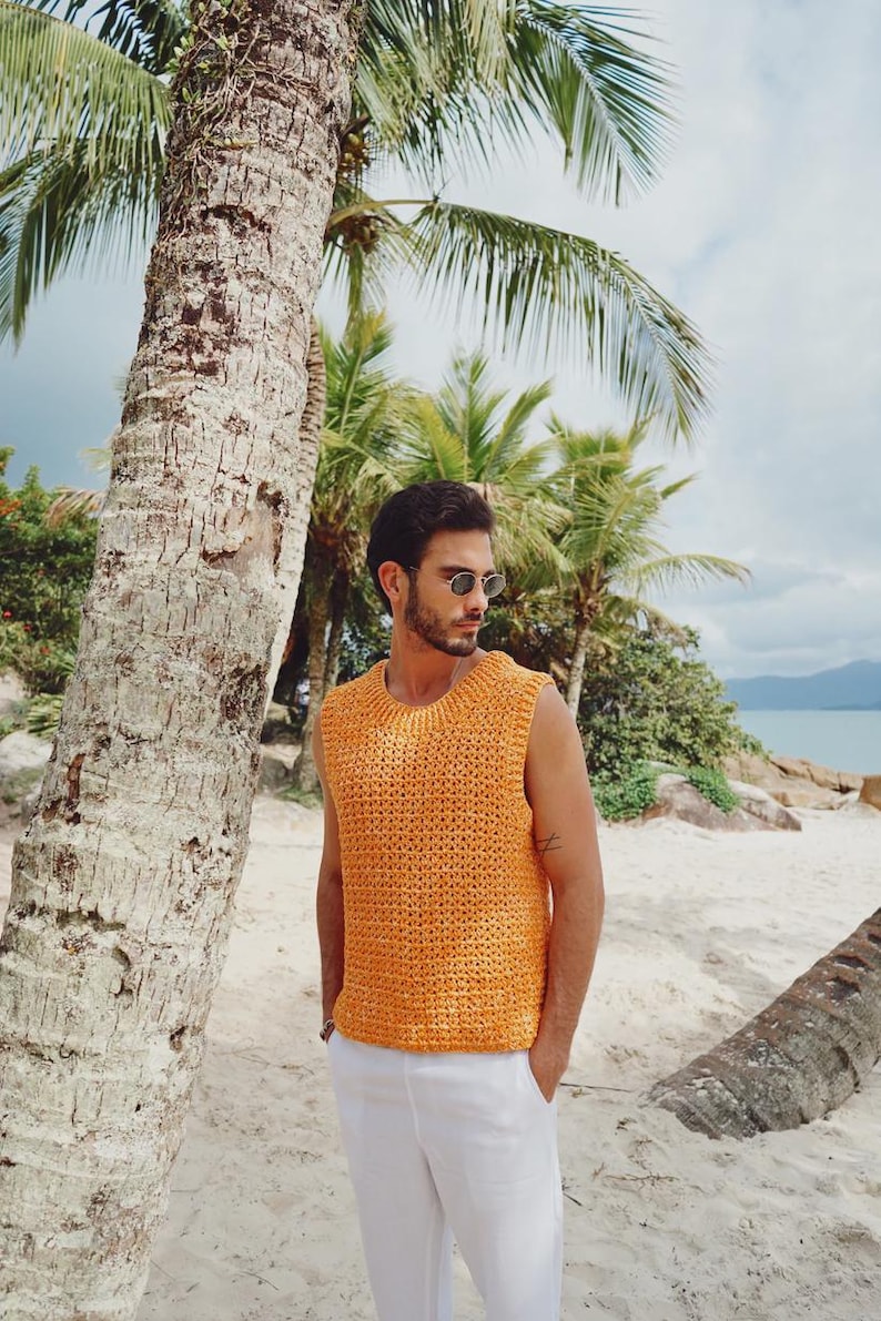 Pu&ograve; includere: Un top smanicato in maglia color arancione brillante con scollo rotondo e un motivo testurizzato a maglia aperta. Il capo &egrave; abbinato a pantaloni bianchi semplici, creando un look essenziale e pulito adatto a climi caldi e ambienti esterni.