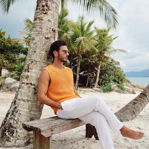 Pu&ograve; includere: Un top senza maniche all'uncinetto color arancione brillante con scollo rotondo e pantaloni bianchi. Il top presenta un motivo a maglia aperta e testurizzata, mentre i pantaloni sono a tinta unita, di colore chiaro e a lunghezza intera.