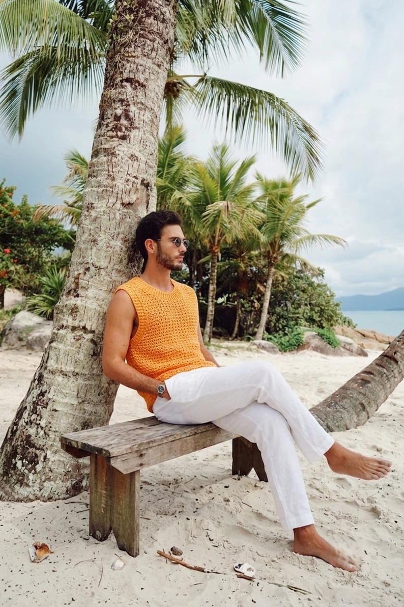 Pu&ograve; includere: Un top senza maniche all'uncinetto color arancione brillante con scollo rotondo e pantaloni bianchi. Il top presenta un motivo a maglia aperta e testurizzata, mentre i pantaloni sono a tinta unita, di colore chiaro e a lunghezza intera.