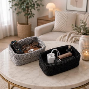 May include: Two rectangular storage baskets made of thick, woven cord. One basket is light gray and contains a black remote control, brown-rimmed glasses, and a white circular tag. The other basket is black and holds white wireless earbuds.