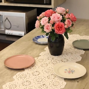 May include: A bouquet of pink and red roses in a dark vase sits on a table runner. Several plates in shades of pink, blue, and green are arranged around the flowers. A microwave is visible in the background.