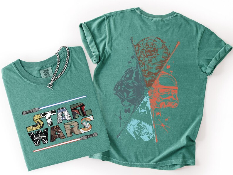 K&ouml;nnte beinhalten: Zwei tealfarbene T-Shirts. Eines gefaltet mit den Worten "STAR WARS" in einer bunten Grafik. Das andere Shirt hat eine Grafik von Darth Vader, einem Sturmtruppler und dem Todesstern. Eine silberne Halskette befindet sich auf dem gefalteten Shirt.