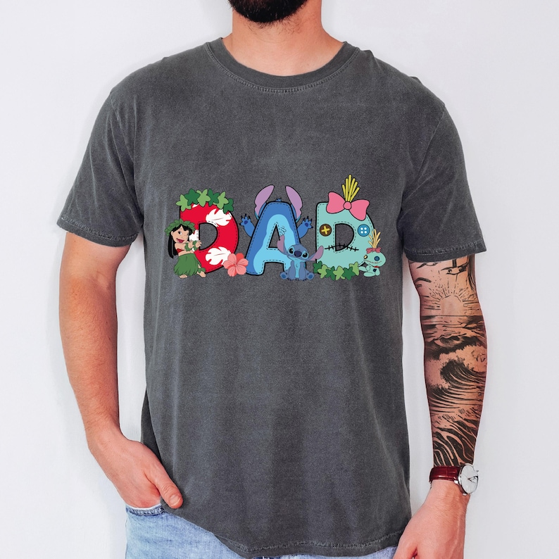 May include: A charcoal gray short-sleeve t-shirt featuring a graphic print that spells the word DAD. The letters are decorated with Lilo and Stitch characters, including Lilo, Stitch, and Scrump, along with tropical flowers and green leaves.