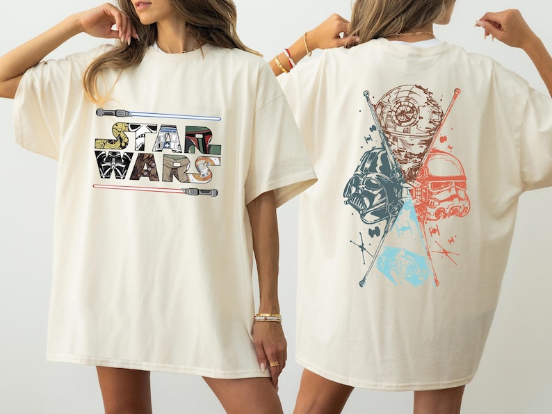 K&ouml;nnte beinhalten: Cremefarbenes T-Shirt mit dem Star Wars-Logo auf der Vorderseite, flankiert von Lichtschwertern. Auf der R&uuml;ckseite sind Darth Vader, ein Sturmtruppler und der Todesstern mit gekreuzten Lichtschwertern abgebildet.