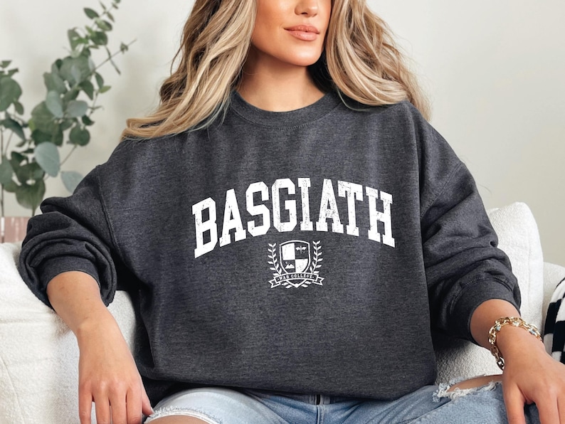 以下が含まれることがあります： 胸に「BASGIATH」の文字が白くかすれた文字でプリントされたダークグレーのスウェットシャツ。その下に「BAR COLLEGE」の文字が入った紋章があります。クルーネックのスタイルのスウェットシャツです。
