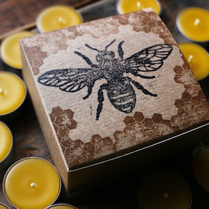 May include: A box of small, round, yellow beeswax candles with a brown paper lid featuring a black bee illustration and a honeycomb pattern.