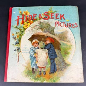 Peut inclure: Livre pour enfants vintage intitulé "Hide & Seek Pictures". La couverture présente une illustration de trois enfants sous un parapluie, avec un arbre et un ciel nuageux en arrière-plan. Le titre est en rouge, avec des fleurs jaunes et du feuillage vert.