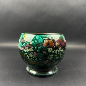 Peut inclure: Un petit bol en verre arrondi présentant un motif tacheté aux couleurs vives. La surface affiche un mélange riche de vert émeraude profond, de vert forêt foncé et de noir, rehaussé de petites taches éparses de blanc, d'or et de rouge foncé.