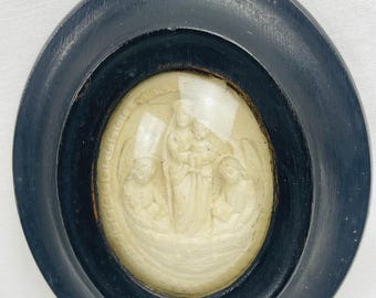 May include: An oval, antique religious relief in a dark blue wooden frame. The relief shows a central figure flanked by two others. The relief is off-white and protected by glass.