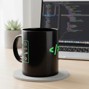 K&ouml;nnte beinhalten: Eine schwarze Kaffeetasse mit gr&uuml;nem Text und Symbolen zum Thema Programmieren. Die Tasse steht auf einem grauen Untersetzer, im Hintergrund ist ein Laptop mit Code zu sehen. Eine kleine Sukkulente ist ebenfalls sichtbar.