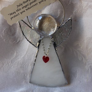 May include: A stained glass angel ornament with a clear glass head, silver wings, and a white body. A red heart pendant hangs from a silver chain. The tag reads "July-Ruby May this angel guide and protect you wherever you go."