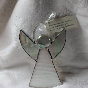 May include: A stained glass angel ornament with iridescent wings and a white body. The ornament has a silver wire loop for hanging and a tag with the text "For He orders His angels to guide and protect you wherever you go. Psalm 91:11".