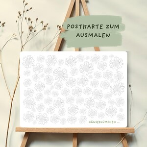 Può includere: Una cartolina bianca con un motivo di contorni di margherite, esposta su un cavalletto di legno. Il testo "POSTKARTE ZUM AUSMALEN" è scritto su uno striscione verde sopra la cartolina. Il testo "GÄNSEBLÜMCHEN ..." è scritto in basso.