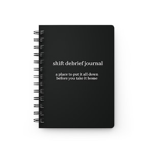 May include: A black spiral-bound journal with the text "shift debrief journal" and the tagline "a place to put it all down before you take it home" in white. The journal is rectangular and has a black cover.