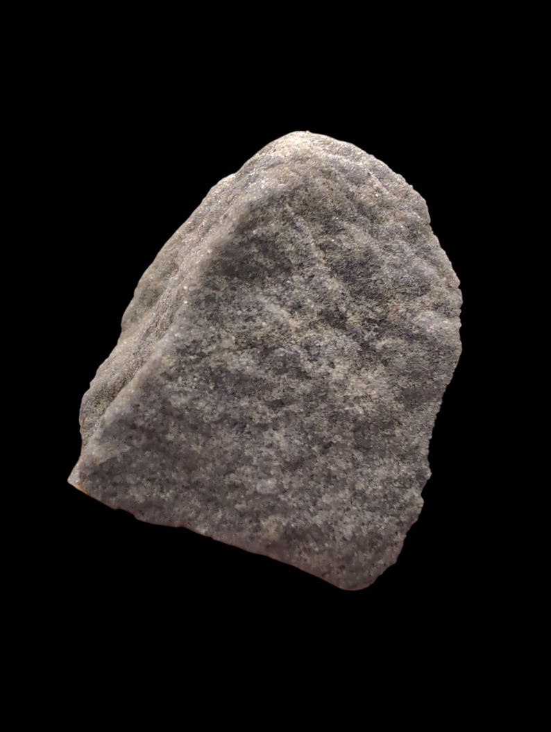 May include: A close-up of a gray rock against a black background. The rock has a rough, textured surface with various shades of gray and white. The shape is irregular, with a slightly rounded top and a jagged edge.